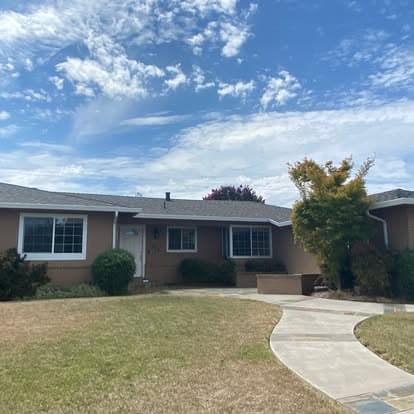 Single-story beige house with lush front yard and concrete pathway under a blue sky.
