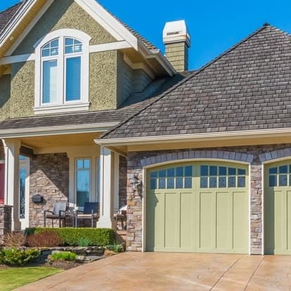 Modern two-story home with stone accents, green garage doors, and landscaped front yard.