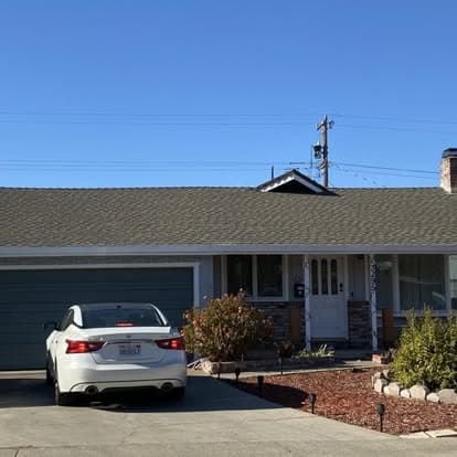 Single-story house with gray exterior, white car parked in driveway, and drought-resistant landscaping.