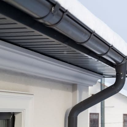 Snow-covered roof gutter system with downspout on a residential building.