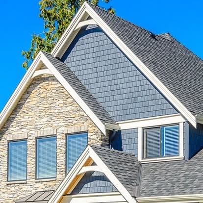 Modern house exterior with gray shingle roof and stone accents under a clear blue sky.