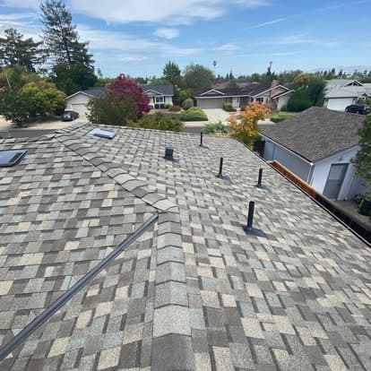 Aerial view of residential rooftops with skylights and chimneys under a clear blue sky.