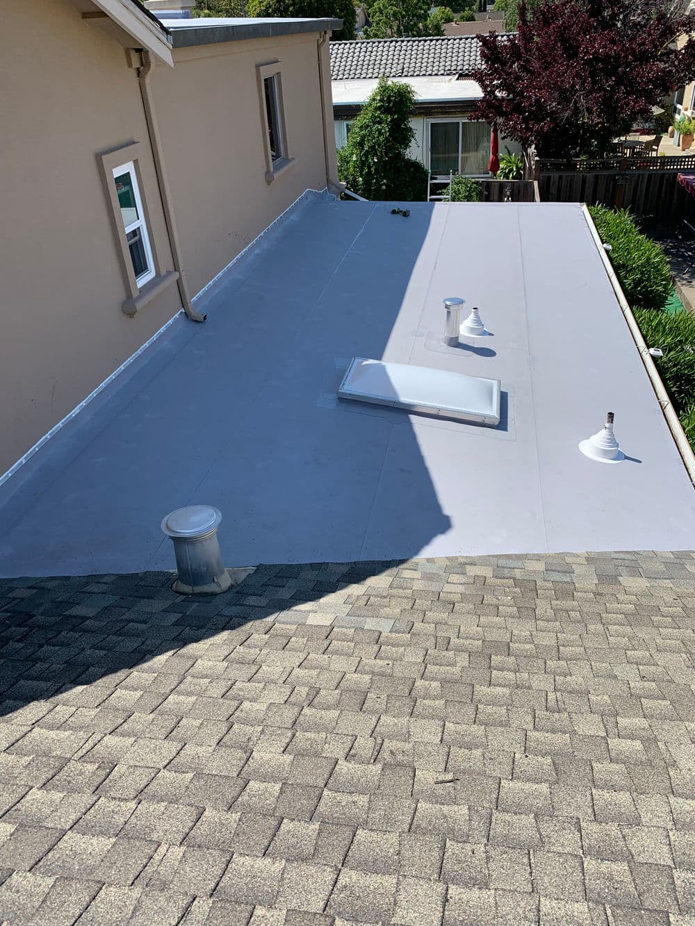 Flat rooftop with skylight and ventilation pipes, viewed from adjacent sloped roof.