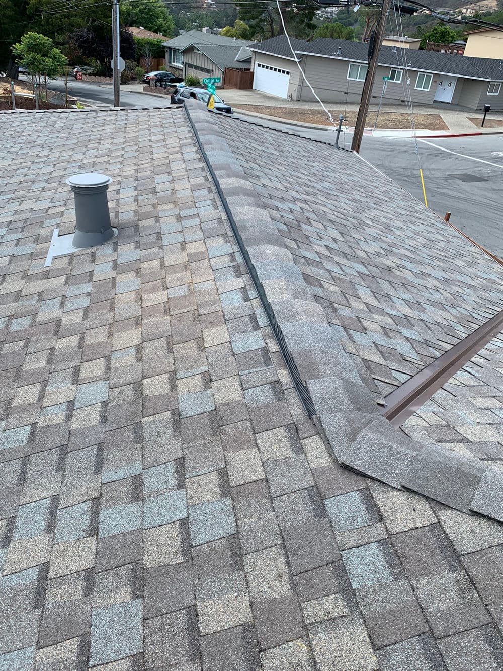 Aerial view of a shingled roof with a metal ridge and surrounding neighborhood.