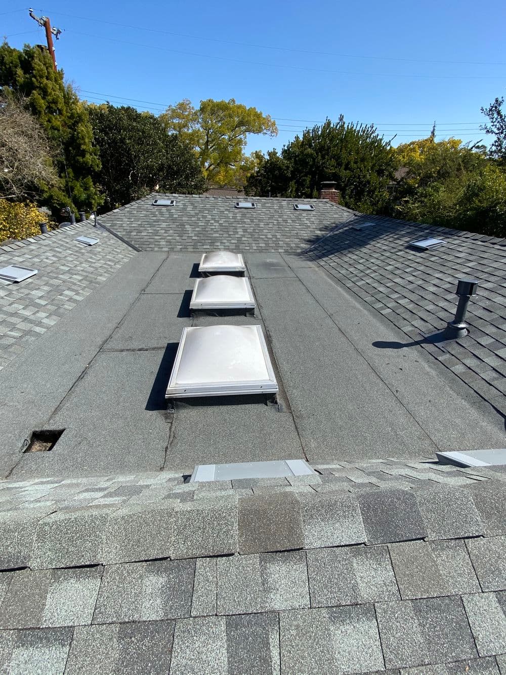 Roof with skylights, gray shingles, and ventilation pipes in a residential area.
