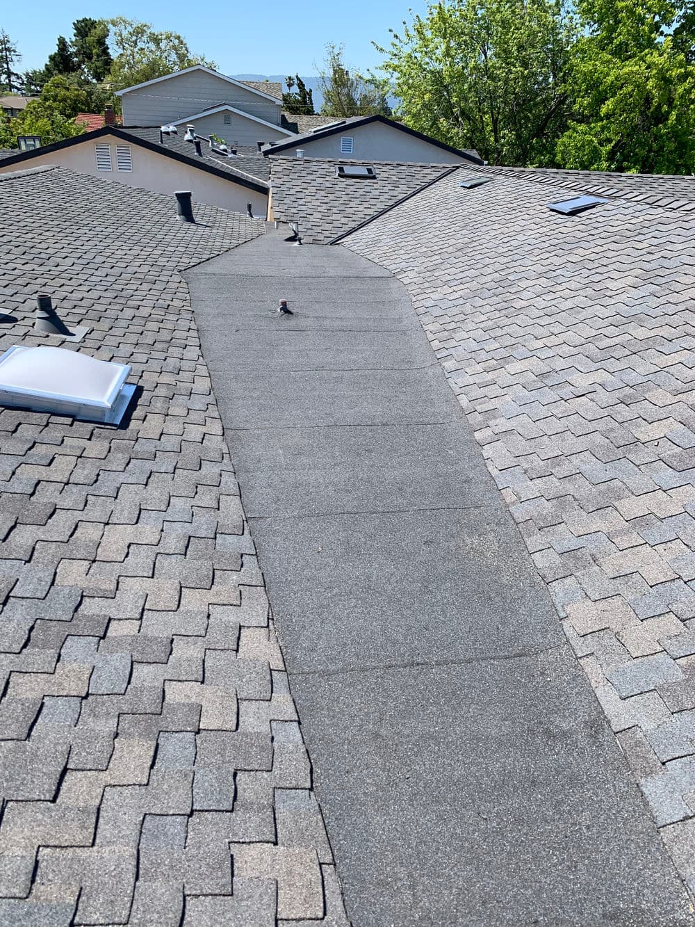Aerial view of sloped asphalt shingle roofs with skylights and clear blue sky.