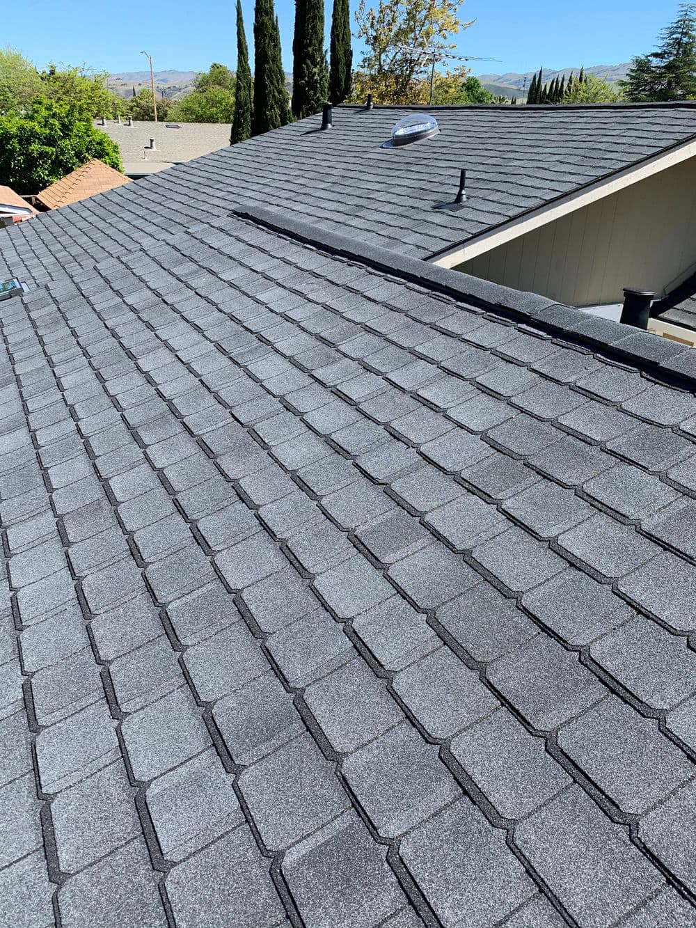 asphalt shingle roof with grey tiles and skylight under clear blue sky