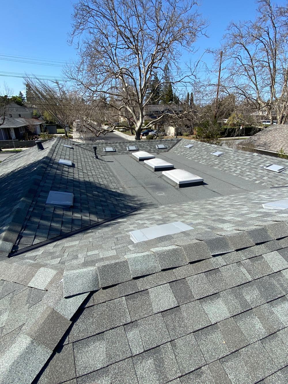 Aerial view of a residential roof with skylights and asphalt shingles on a sunny day.