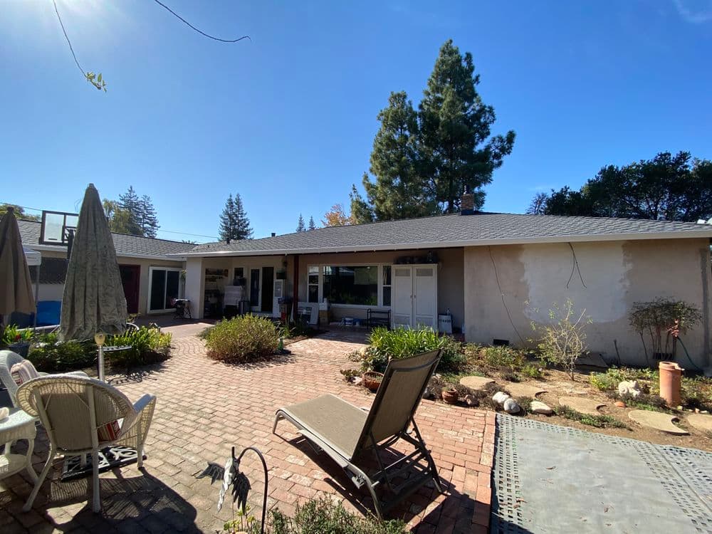 Sunny backyard with patio chairs, a lounge chair, and landscaped garden near a house.