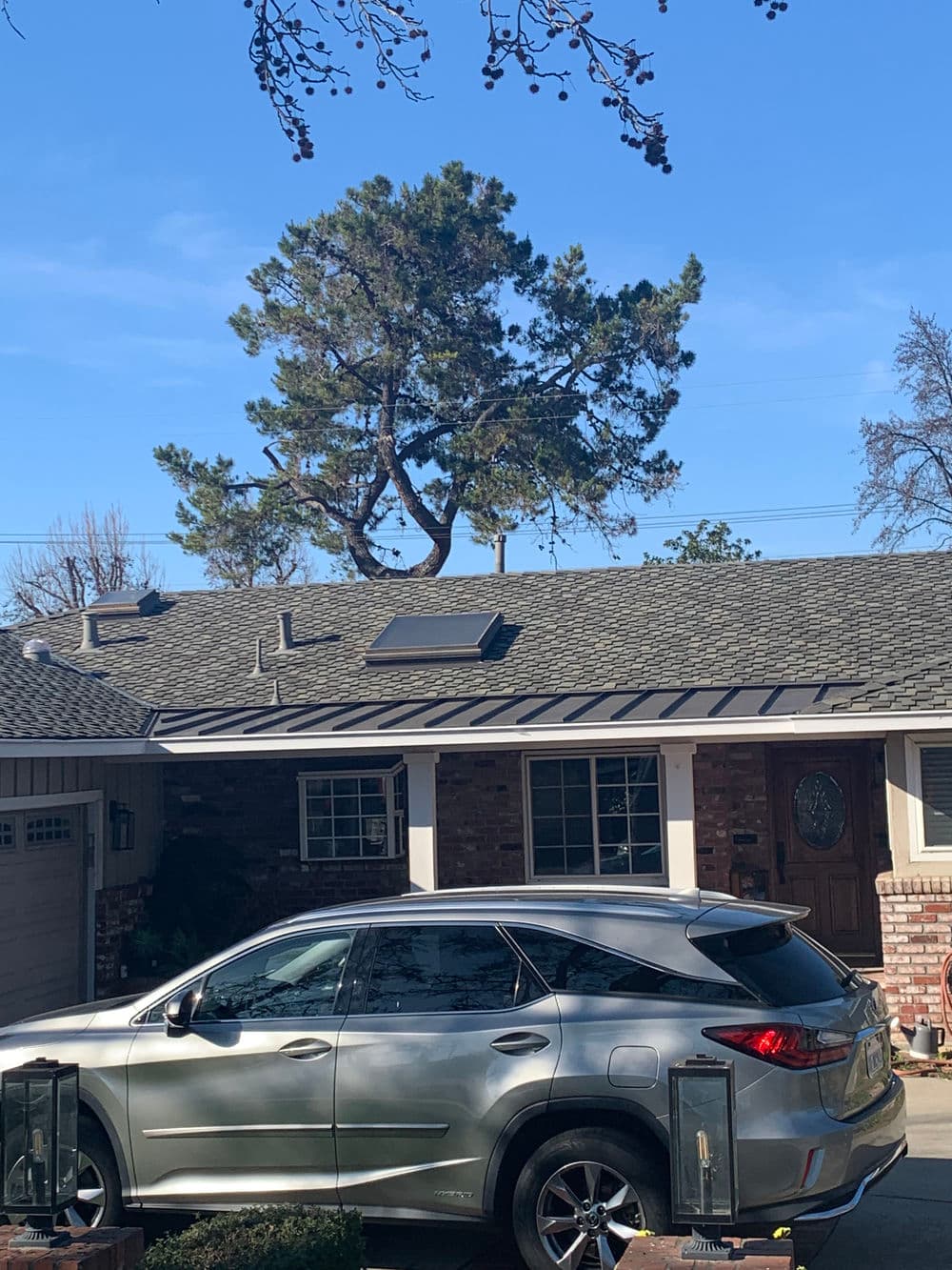 Silver SUV parked in front of a suburban home with solar panels and a large green tree.