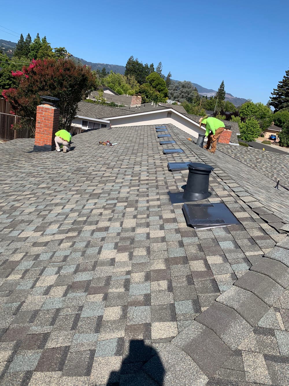 Roofing crew working on a residential roof installation with mountains in the background.